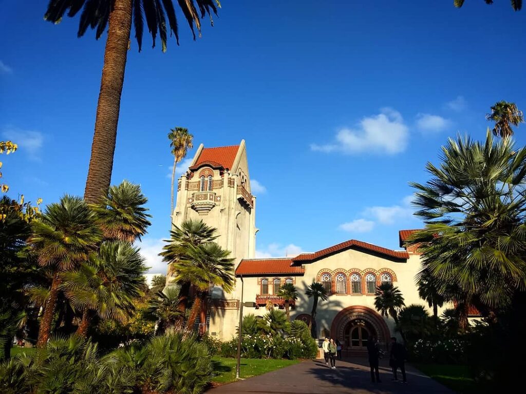 a Spanish style building surrounded by palm trees, grass, and a walkway