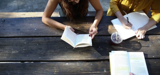 three people read and write sitting at a wooden picnic bench