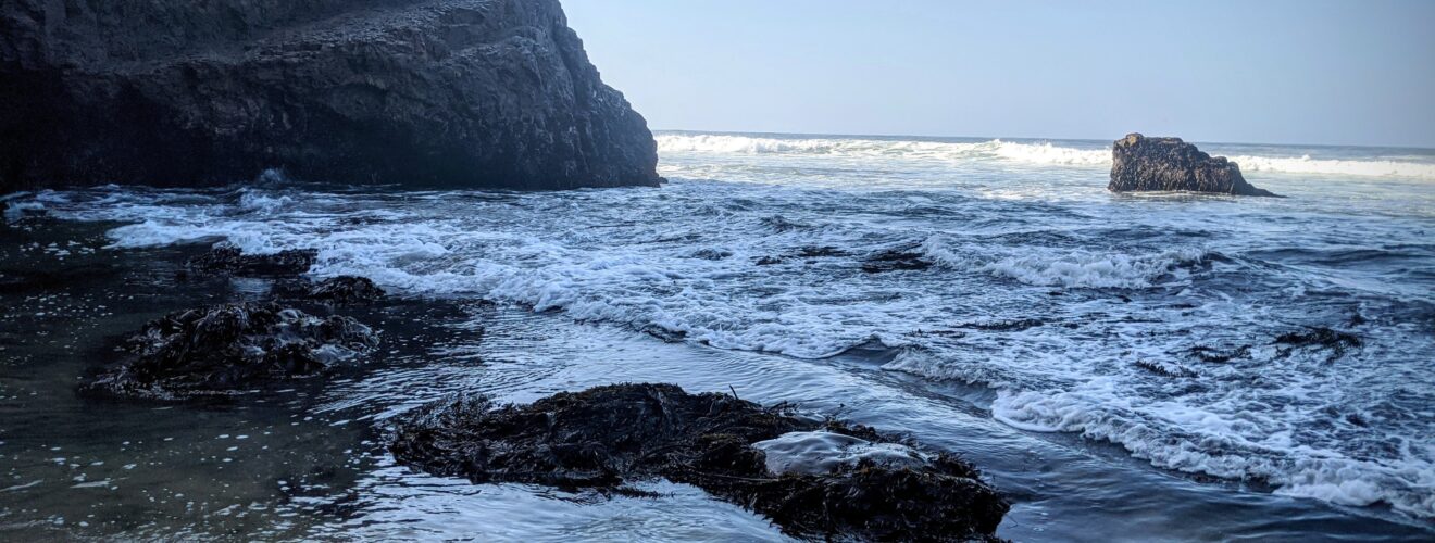 rocky cliff, beach, and waves in shdows